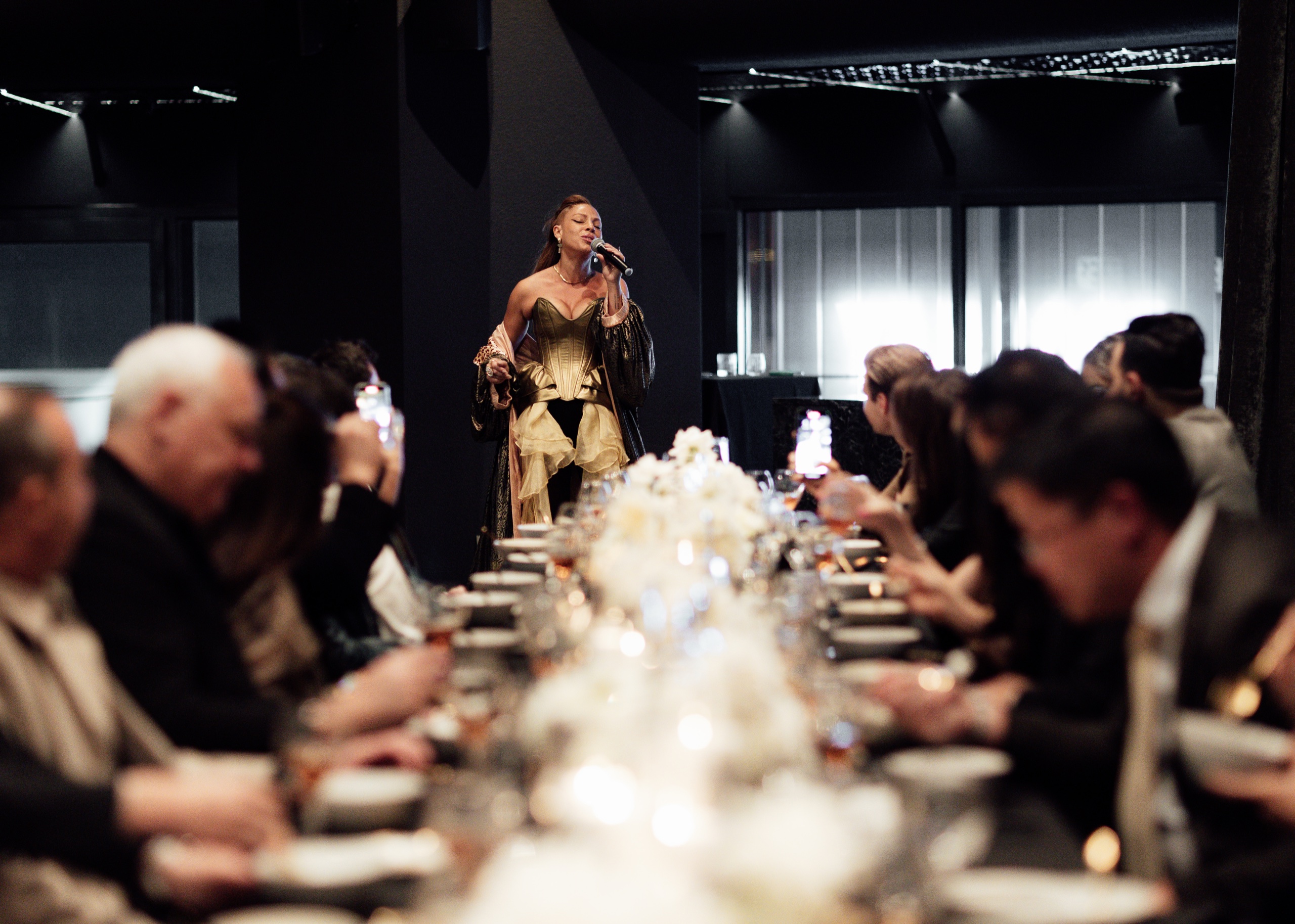 Guests at a long dinner table with a vocalist performing at the far end.